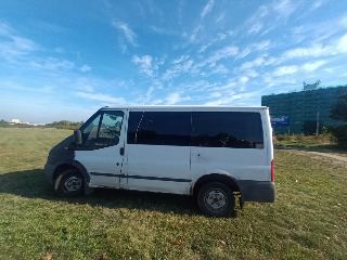 Fotografie bílé dodávky Ford Transit zaparkované na travnaté ploše pod širým nebem.