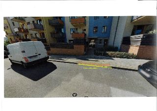 Fotografie ulice s vyznačeným úsekem označeným žlutou čarou a textem 'V 12c v délce snížení', u chodníku stojí bílá dodávka a černý automobil