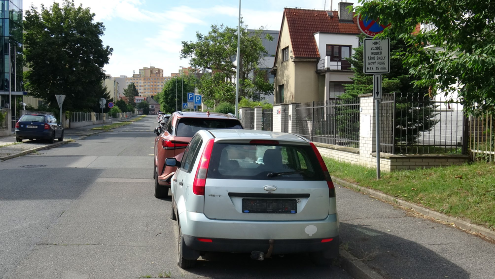 Fotografie ulice s dopravním značením. Na dopravní značce je uvedeno: 'PO-PÁ', 'MIMO VOZIDEL RODIČŮ ŽÁKŮ ŠKOLY NOVÝ PORG MAX. 15 min.' a šipka směřující dolů.