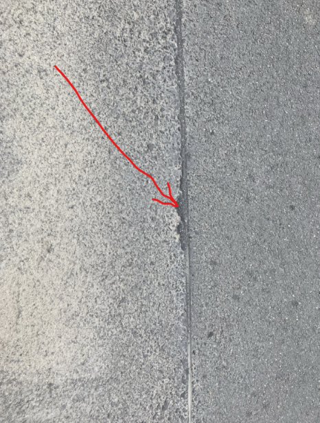 Detailní fotografie povrchu vozovky nebo chodníku s vyznačeným spárem či trhlinou.