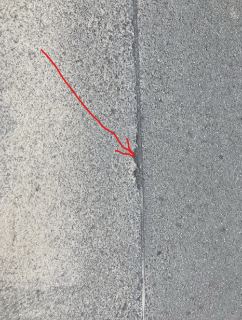 Detailní fotografie povrchu vozovky nebo chodníku s vyznačeným spárem či trhlinou.