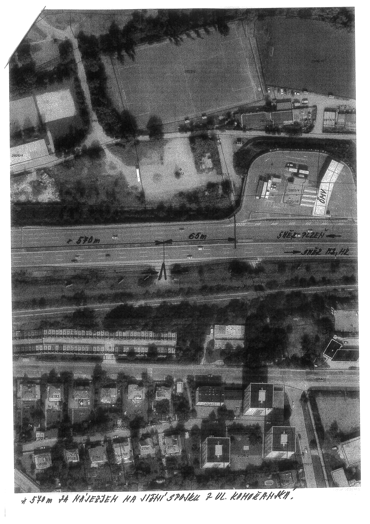 Letecký snímek (ortofoto) území s vyznačeným měřením vzdáleností na silnici. V obrázku jsou ručně psané poznámky: '570m', '65m', 'SMĚR PLZEŇ', 'SMĚR HZ, HL', 'OMV' (u čerpací stanice) a text v dolní části: '* 570m ZA NÁJEZDEM NA JIŽNÍ SPOJKU Z UL. KOMOŘANSKÁ.'