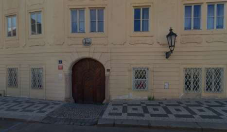 Fotografie budovy s domovním číslem orientačním 4 (červená tabulka s bílým číslem 4 vedle vchodu). Nad vchodem je umístěn domovní znak (reliéf).