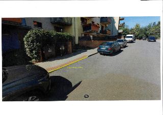 Fotografie ulice s vyznačeným úsekem obrubníku žlutou čárou a popisem 'V 12c v délce v snížení', u chodníku parkují vozidla, vlevo popelnice a zeleň, v pozadí…