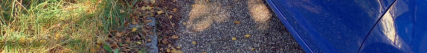 Fotografie exteriéru, pravděpodobně detail podvozku nebo boční části modrého vozidla parkujícího na zpevněné ploše.