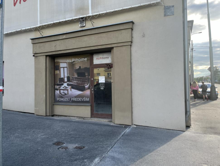 Fotografie budovy s prodejnou ALPIhome, která slouží jako dokumentace stavu nemovitosti nebo lokality.