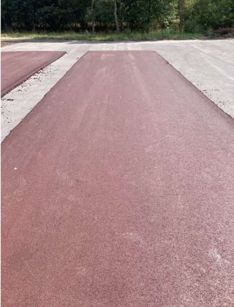 Fotografie nově položeného červeného asfaltového povrchu na pozemku.