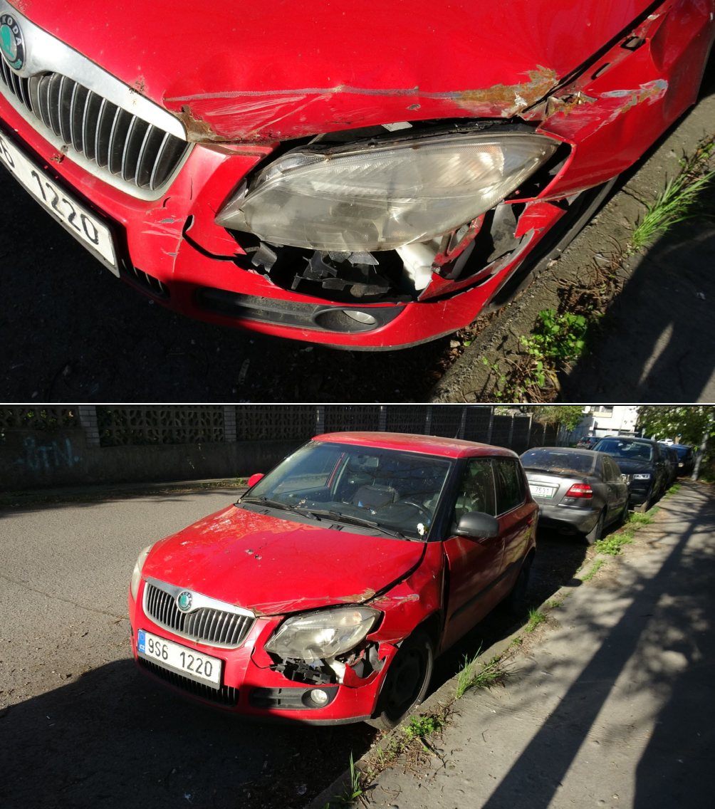 Fotografie poškozeného červeného osobního automobilu značky Škoda (pravděpodobně model Fabia II) zaparkovaného u krajnice. Na registrační značce je čitelný text: '9S6 1220'. Vozidlo vykazuje viditelné poškození přední části, zejména v oblasti levého předního světlometu, nárazníku a kapoty, kde je patrná i koroze.