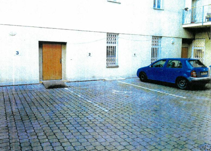 Fotografie exteriéru budovy s vyznačenými parkovacími místy.