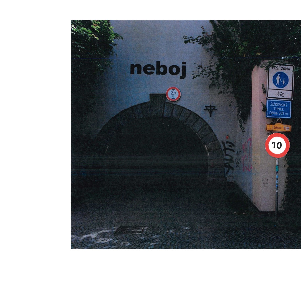 Fotografie vstupu do Žižkovského tunelu. Nad vchodem je nápis 'neboj' a dopravní značka omezující výšku vozidel na 2,7 m. Na pravé straně jsou umístěny dopravní značky: 'PEŠÍ ZÓNA', symbol pro cyklisty, modrá tabule s nápisem 'ŽIŽKOVSKÝ TUNEL Délka 303 m', žlutá tabule 'Žižkov' a kruhová značka s číslem '10'.