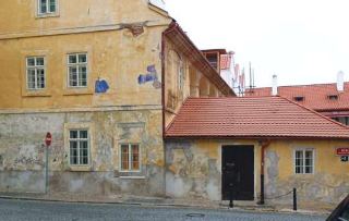 Fotografie budovy s omítkou v havarijním stavu. Na pravé straně budovy je umístěna červená orientační tabulka s bílým textem 'ŘÍČNÍ' a číslem popisným '1'.