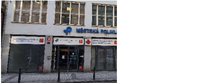 Fotografie budovy Městské polikliniky. Na fasádě je nápis 'MĚSTSKÁ POLIKLINIKA' a logo. Nad vchody jsou umístěny informační tabule s texty: 'LÉKÁRENSKÁ POHOTOVOST', 'MĚSTSKÁ POLIKLINIKA' a 'CENTRUM ZDRAVOTNICKÉ ZÁCHRANNÉ SLUŽBY'.