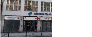 Fotografie budovy Městské polikliniky. Na fasádě je nápis 'MĚSTSKÁ POLIKLINIKA' a logo. Nad vchody jsou umístěny informační tabule s texty: 'LÉKÁRENSKÁ POHOTOV…