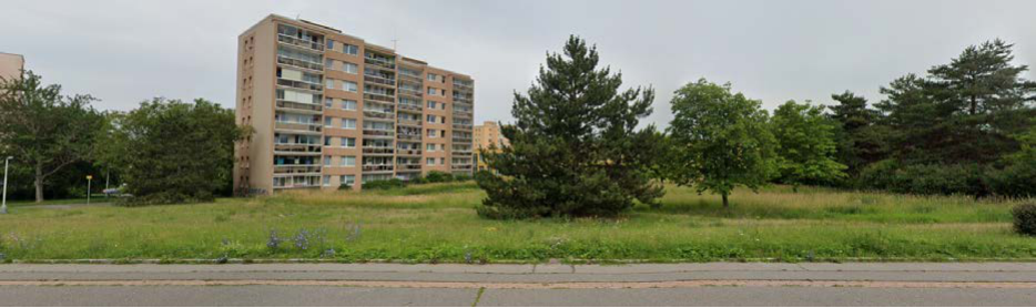 Fotografie pozemku s panelovým bytovým domem v pozadí, pravděpodobně sloužící jako dokumentace stávajícího stavu území.