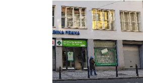 Fotografie budovy s lékárnou. Na budově je nápis 'KLINIKA PRANA'. Nad vchodem do lékárny je zelený nápis 'Lékárna Na Spojce'. Na výloze vpravo je zelený informační panel s textem: 'Lékárna Na Spojce. Otevírací doba: Po-Pá 8:00-18:00. Víkendy a svátky zavřeno. Tel.: 222 211 880'.