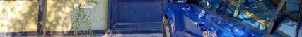 Fotografie modrého osobního automobilu zaparkovaného u zdi budovy.