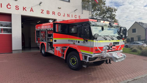 Fotografie hasičského vozu před budovou hasičské zbrojnice.
