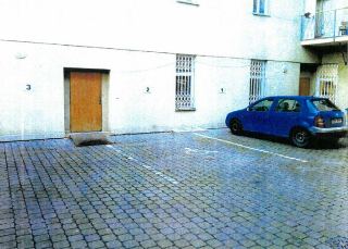 Fotografie budovy s parkovištěm, na které jsou označení '3', '2' a '1' u vchodů/oken a parkovací stání s vyznačeným symbolem pro invalidy, na parkovišti stojí…