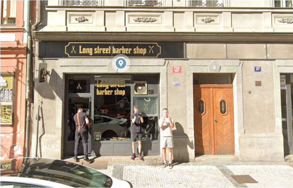 Fotografie budovy s provozovnou 'Long street barber shop'. Na fasádě je viditelné orientační číslo 27 a červená tabulka s číslem popisným 734.