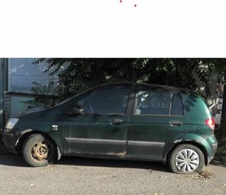 Fotografie tmavě zeleného osobního automobilu zaparkovaného u krajnice, vozidlo má zjevně poškozená (defektní nebo prázdná) kola.