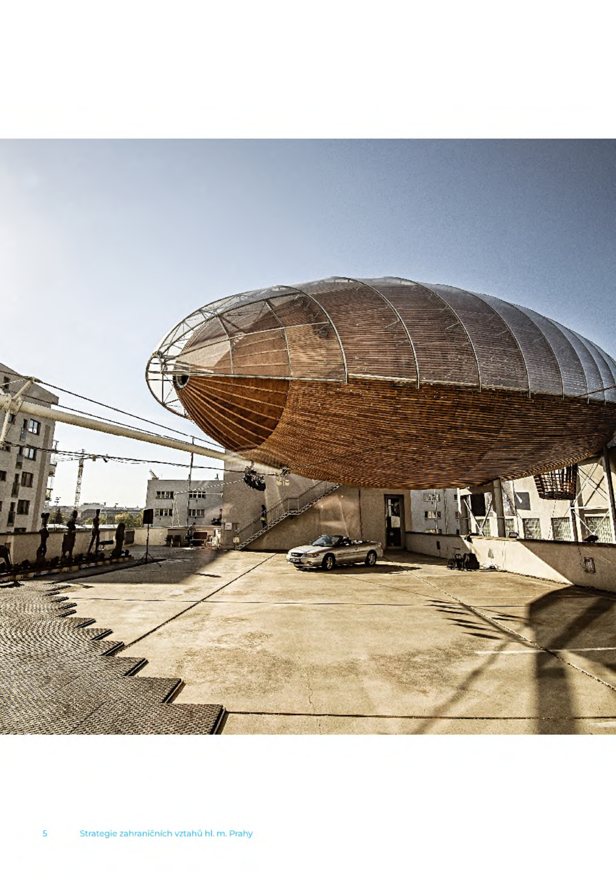 Fotografie umělecké instalace (vzducholoď Gulliver) na střeše budovy DOX v Praze. V dolní části text: '5 Strategie zahraničních vztahů hl. m. Prahy'