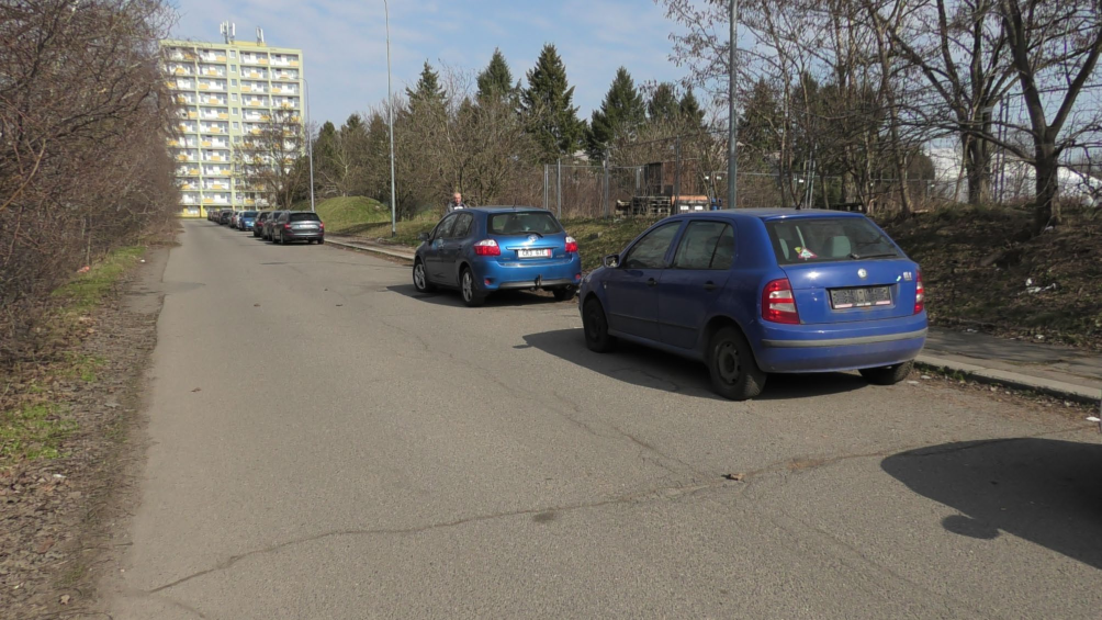 Fotografie pozemku a přilehlé komunikace s parkujícími vozidly.