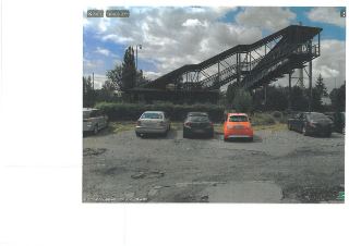 Fotografie exteriéru (pravděpodobně z mapové aplikace Mapy.cz), zachycující kovovou lávku nebo konstrukci nad parkovištěm s několika automobily. V pravém dolní…
