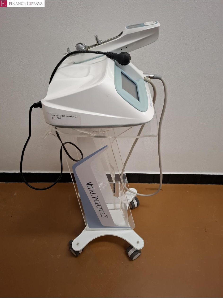 Fotografie kosmetického přístroje na stojanu s označením 'VITAL INJECTOR 2'. Na štítku přístroje je uvedeno: 'Name: Vital Injektor 2', 'SN: 007'. V levém horním rohu je logo 'FINANČNÍ SPRÁVA'.