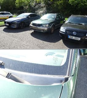 Fotografie automobilů parkujících na odstavné ploše, včetně detailu čelního skla zeleného vozu Subaru s nápisem výrobce Pilkington a homologačními údaji na skl…