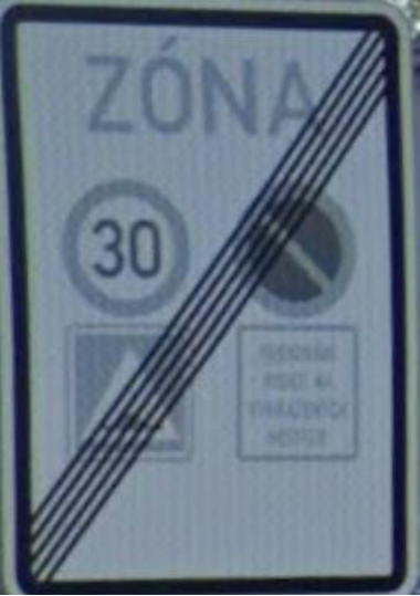 Dopravní značka ukončující zónu s omezením. Obsahuje text 'ZÓNA' a přeškrtnuté symboly: omezení rychlosti na 30 km/h, zákaz zastavení, symbol přechodu pro chodce a doplňkovou tabulku s textem 'PŘESNĚ PŘEJEŤ NA VYHRAZENÝCH MÍSTECH'.